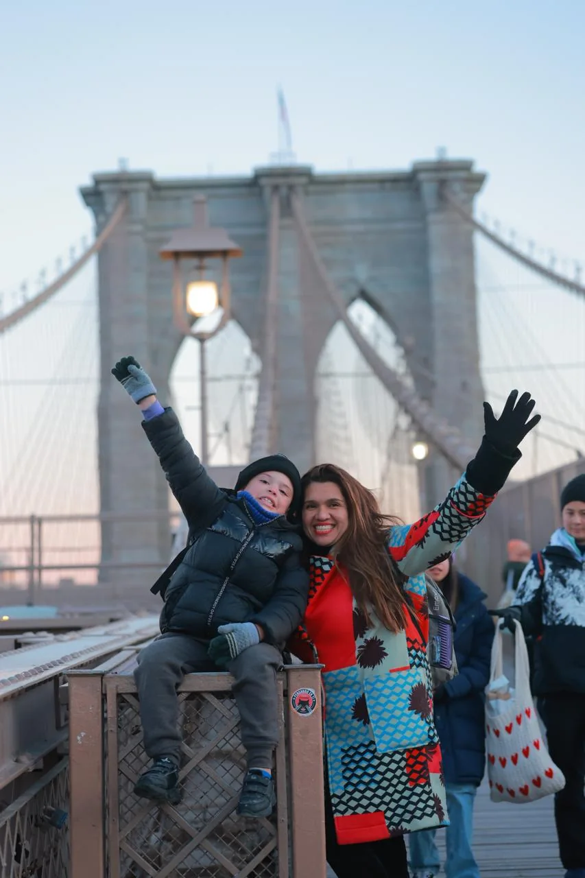 Mey Medina y su hijo con los brazos levantados en el puente de Brooklyn, Nueva York